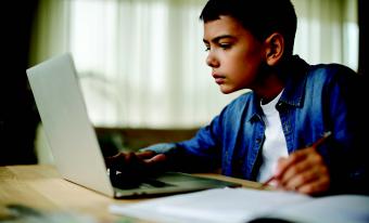 Kid using laptop and writing notes