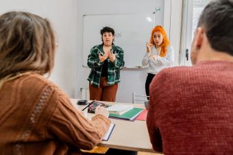 A woman interprets for a Deaf woman during a presentation to two peers/