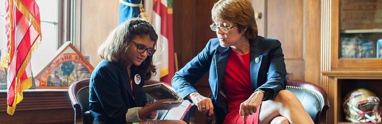 Senator speaking with child in Congressional office looking at assistive technology device
