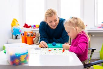 Female educator sitting at a table working with young female child